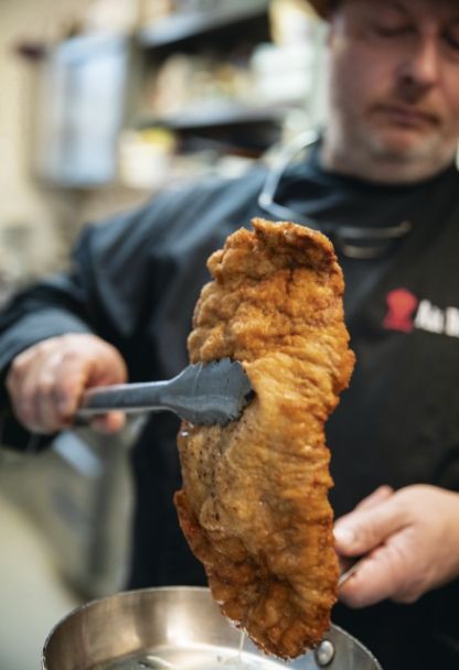 Fertiges Schnitzel wird mit einer Zange aus der Pfanne gehoben